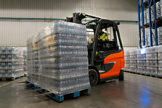 Driver in a forklift carrying two pallets of product in a warehouse