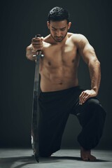 Asian man, kneeling and ninja sword in studio for wellness, calm and exercise for martial arts. Blade, training and self defense by black background for karate and battle for samurai in dojo or Japan © Lumeez23/peopleimages.com