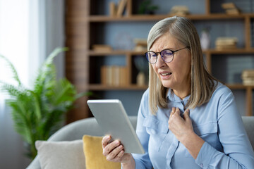 Elderly woman having a virtual medical consultation on a tablet, expressing concern and pain. Online health examination and patient care.