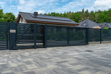 A modern panel fence in anthracite color, visible sliding gate to the garage and a slab driveway.