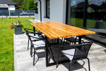 A modern table made of raw wood covered with yacht varnish, standing on the garden terrace.