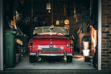 Little red classic Austin Healy parked up in a tight garage in evening sunlight.