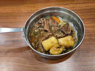 Close Up of Korean Galbi Jjim (Braised Beef Short Ribs) and korean tteokbokki in a Stainless Steel Pan on a Wooden Table
