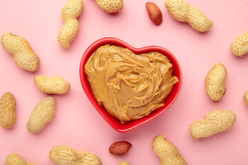 Heart shaped bowl with peanut butter and peanuts on pink background. Creamy peanut pasta in small bowl.