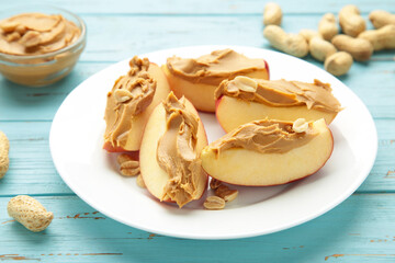 Slices of fresh apple with peanut butter on plate on blue background.