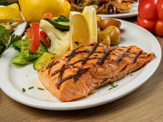 a dinner plate filled with a portion of grilled salmon filet and assorted vegetables in a restaurant setting