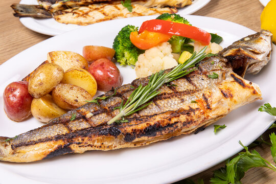 a dinner plate filled with a grilled whole head on branzino fish filets and assorted vegetables in a restaurant setting