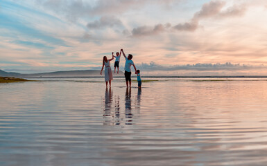 Fototapeta premium Sunset, holding hands and family at beach on vacation, adventure or holiday together for bonding. Summer, fun and parents walking in ocean, sea or waves with children on tropical weekend trip.