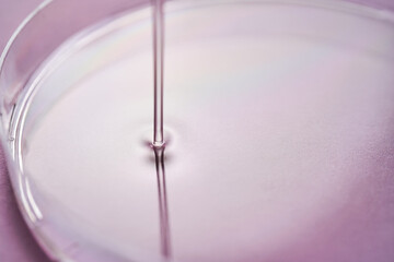 Serum or cosmetic oil flows into a transparent bowl on a purple background.