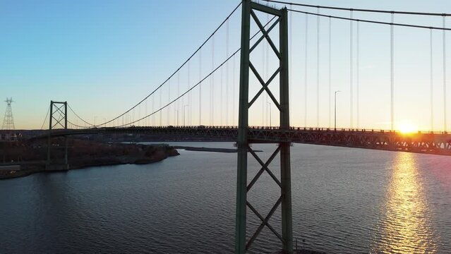Aerial view of A. Murray MacKay Bridge, Halifax, NS. Cinematic drone shot of a suspension bridge with cars and trucks in the evening at sunset.