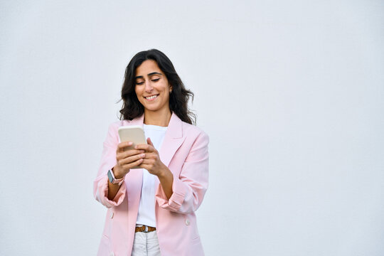 Smiling young middle eastern Israel businesswoman using smartphone mobile phone online app for work isolated on white background. Indian or arabic woman in business suit holding cellphone. Copy space