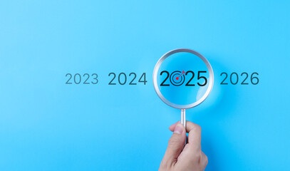 The 2025 New Year business goals concept. Hand holding a magnifying glass highlighting year 2025...