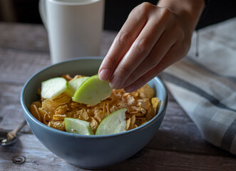 Concept of taking or grabbing food with hands, feminine mature Mexican hands. pieces of green apple on top of corn flakes as part of breakfast