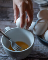 Concept of taking or grabbing food with hands, feminine Mexican hands. Breaking egg into a white cup to stir it with a fork