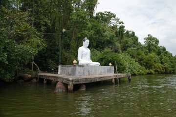 Beruwala,Sri Lanka. 02 february 2023 .white Buddha figure sits over lake. Background beautiful nature palm trees,blue sky. Asia travel and religion concept