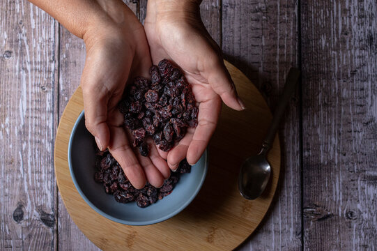 Concept of taking or grabbing food with hands, feminine Mexican hands. Raisins in two hands  on a wooden cutting board and in a bue bowl with a spoon on the side, top view horiontal or lay flat image