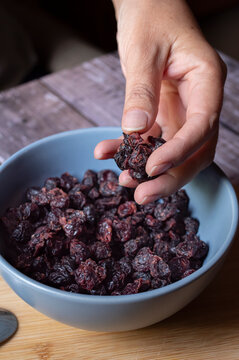 Concept of taking or grabbing food with hands, feminine Mexican hands, raisins in a blue bowl vertical angle view.