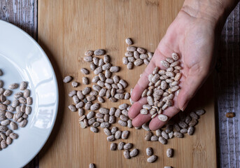 Concept of taking or grabbing food with hands, feminine Mexican hands. Raw beans on a wooden cutting board and on a white plate, horizontal top view