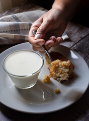 Concept of taking or grabbing food with, feminine Mexican hands. corn bread or cake on a white plate with milk on a rustic wooden table. Top View