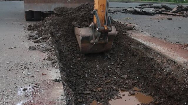 Excavator digs trench in the construction site, close up backhoe digger