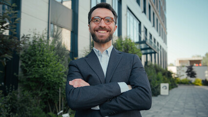 Successful happy man businessman confident pose crossed hands outdoors putting on glasses male business portrait entrepreneur leader ceo wear eyeglasses formal suit smiling looking at camera in city