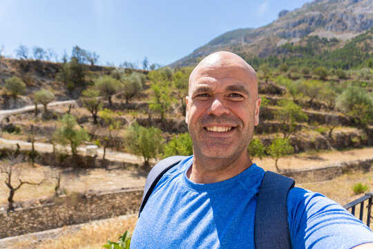 Male hiker takes a selfi outdoors, with mountains and trees on background. 