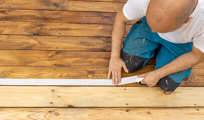 A worker carefully applies painters tape to a newly stained wooden deck, ensuring clean lines for a...