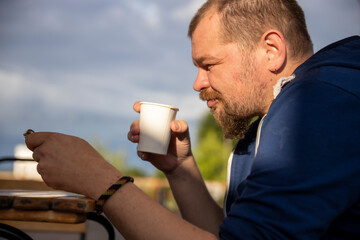 A man sits at a table outdoors, enjoying a cup of coffee on a sunny afternoon. He appears to be in...