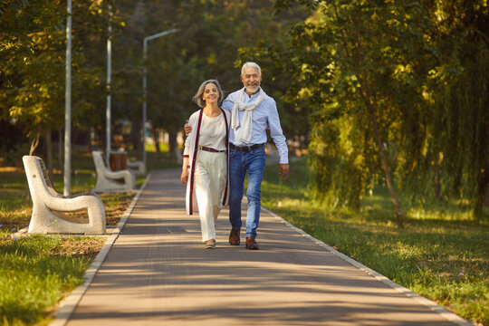 Happy smiling senior couple family hugging while walking in summer city park enjoying retirement and spending time together in nature. Romance, love. care and elderly people relationship concept.