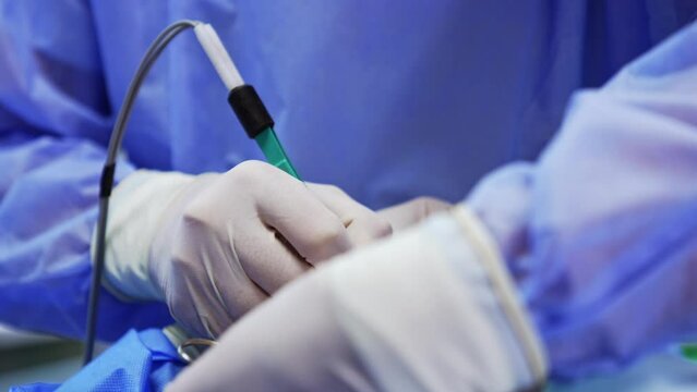Unrecognized doctor in white latex gloves uses electric device tool at operation. Close up. Surgeon at work.