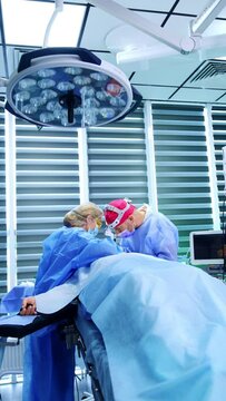 Medics stand at the head of the patient at operation. Surgeon performs procedure for thyroid eye disease. Vertical video.