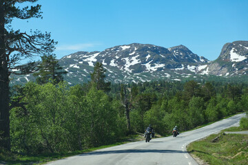 Two motorcycles ride along a mountain road in Norway