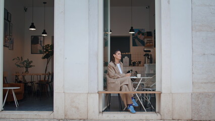 Gorgeous freelancer resting cafe table looking on urban street. Elegant woman