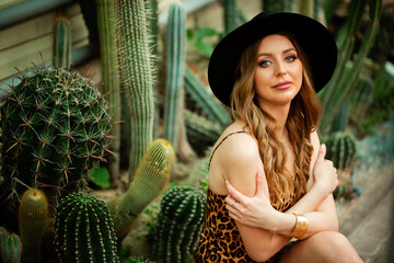 beautiful stylish young woman in brown dress in desert among the cacti, wearing a hat, traveling in Africa on safari, exploring nature, sunny summer, traveler on