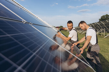 Two skilled workers or craftsmen wearing working gray uniforms, technicians are installing solar panels on a solar farm for clean energy and electricity supply