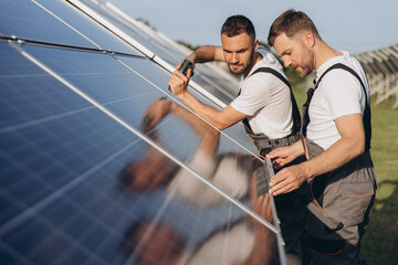 Two skilled workers or craftsmen wearing working gray uniforms, technicians are installing solar panels on a solar farm for clean energy and electricity supply