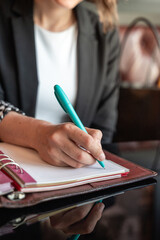 Close-up of a female hand writing on an blank notebook with a pen. Leather notebook on a black...