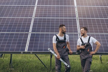 Two bearded technicians professionals servicing solar farm panels discuss finishing work