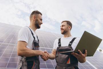 Energy specialist using digital tablet reading information to check the efficiency of solar panel construction. Green energy jobs. Technology. Two solar power plant workers hand shake
