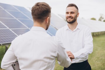 Two technical expert partners in solar photovoltaic panels shake hands, remote control performs...