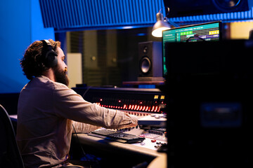 Music producer customizes and edits songs to generate new tunes, adding sound effects to refine rhythm on recordings. Professional technician in audio engineering works in control room.