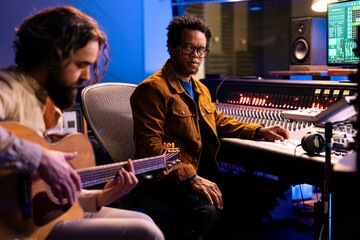 Singer recording electro acoustic guitar in professional music studio, playing musical instrument...