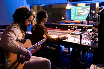 Skilled artist musician recording his guitar sounds in professional studio, using electro acoustic...