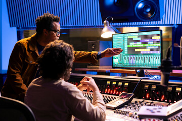 Diverse music experts mixing sounds on audio console and equalizer, adding sound effects and...