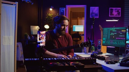 Musical producer doing online guitar lessons with smartphone vlog, recording himself singing and playing acoustics. Artist teaching people how to play and tune instrument with strings. Camera B.