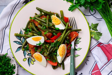 Warm vegetable salad with green beans and boiled eggs on a plate with an ornament..top veiw.selective focus