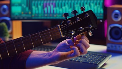 Musical performer tuning his guitar by twisting the knobs, preparing to play acoustic instrument in...