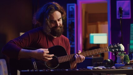Obraz premium Artist playing guitar and uses DAW software interface to create music, looking at mastering controls on computer screen. Musician recording soundtracks with tools, acoustical engineering. Camera A.