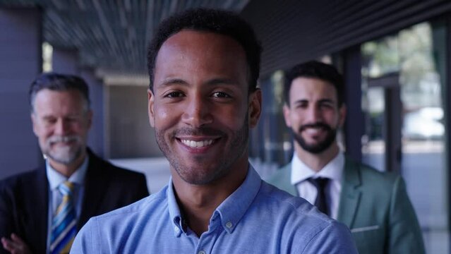 Smiling American black business man in suits looking happy at camera outside office building with diverse team. Successful partners at background. People confident posing cheerful for portrait. 