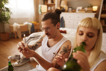 Caucasian couple smoking marijuana joint and drinking beer at home